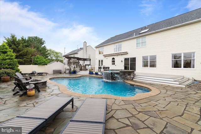 view of swimming pool featuring a fire pit, a patio area, a fenced backyard, a pool with connected hot tub, and a storage shed