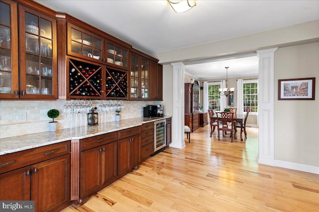 bar area with light wood-style flooring, decorative columns, tasteful backsplash, and baseboards