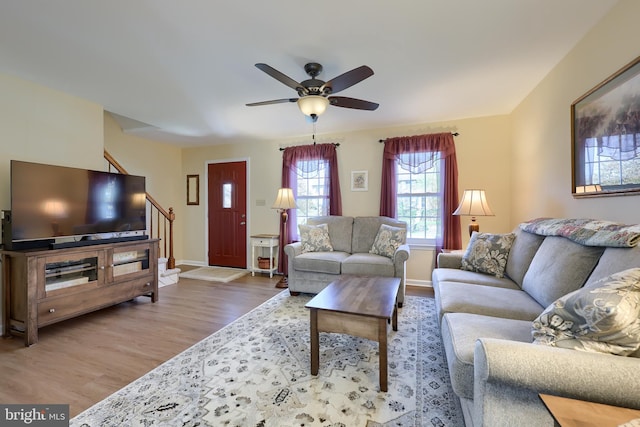living room featuring stairs, baseboards, ceiling fan, and wood finished floors