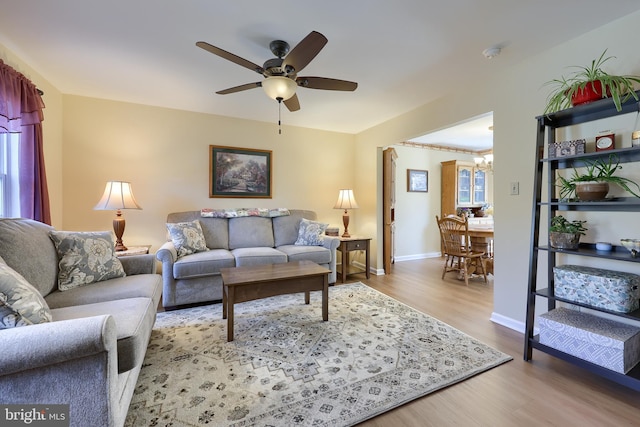living area with baseboards, ceiling fan with notable chandelier, and wood finished floors