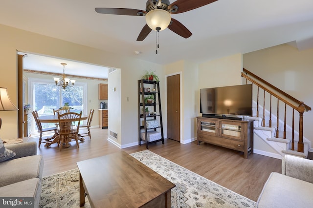 living room featuring visible vents, stairs, baseboards, light wood-type flooring, and ceiling fan with notable chandelier