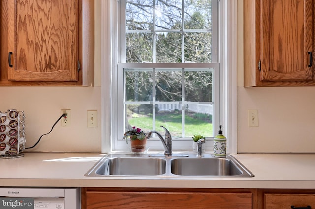 kitchen with a sink, brown cabinetry, and dishwashing machine