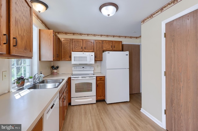 kitchen with brown cabinets, light countertops, a sink, light wood-style floors, and white appliances