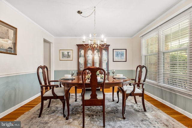 dining space with baseboards, ornamental molding, wood finished floors, and a chandelier