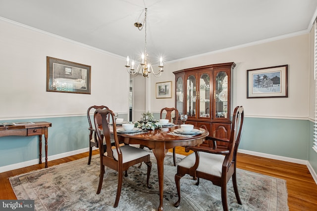 dining area with baseboards, ornamental molding, wood finished floors, and a notable chandelier