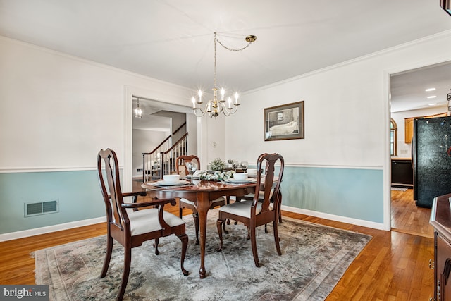dining space with visible vents, crown molding, wood finished floors, stairway, and a notable chandelier