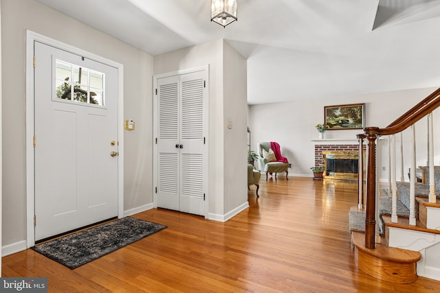 entrance foyer featuring baseboards, a brick fireplace, wood finished floors, and stairway