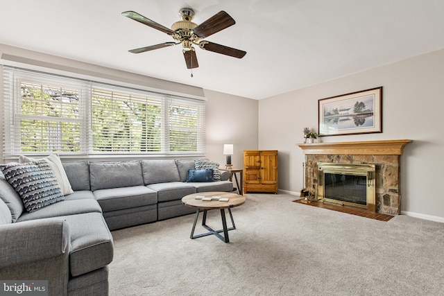 carpeted living area with a ceiling fan, baseboards, and a stone fireplace
