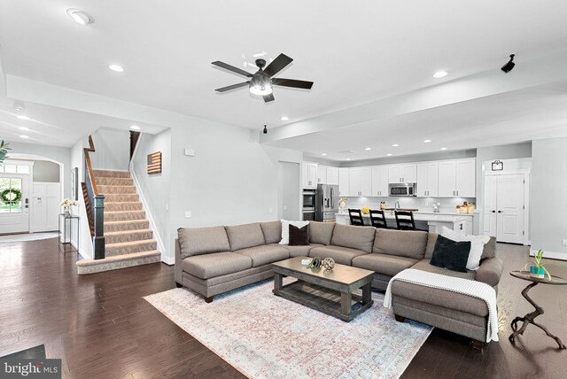 living room with baseboards, dark wood-style flooring, a ceiling fan, and stairs