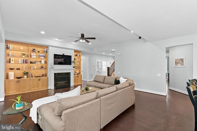 living room featuring stairs, baseboards, ceiling fan, a fireplace with flush hearth, and dark wood finished floors