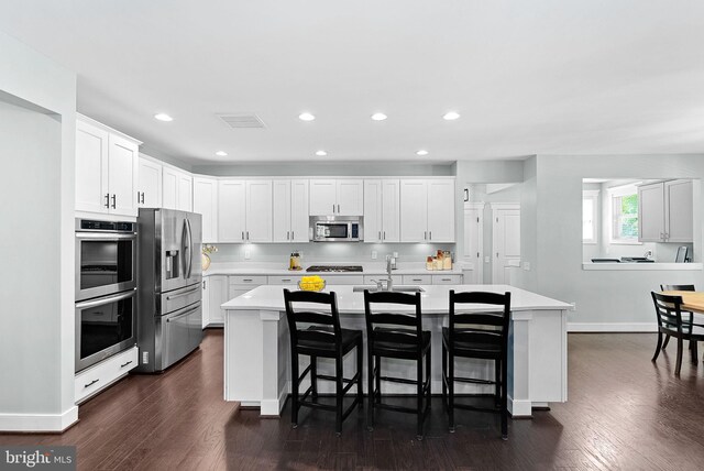 kitchen with a kitchen island with sink, a breakfast bar area, light countertops, baseboards, and stainless steel appliances