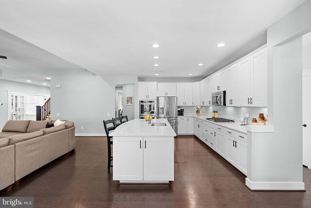 kitchen with appliances with stainless steel finishes, white cabinetry, open floor plan, baseboards, and a kitchen bar