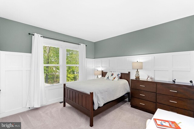 bedroom with light colored carpet, wainscoting, and a decorative wall