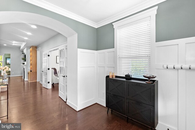 corridor featuring crown molding, arched walkways, a wainscoted wall, a decorative wall, and dark wood-type flooring