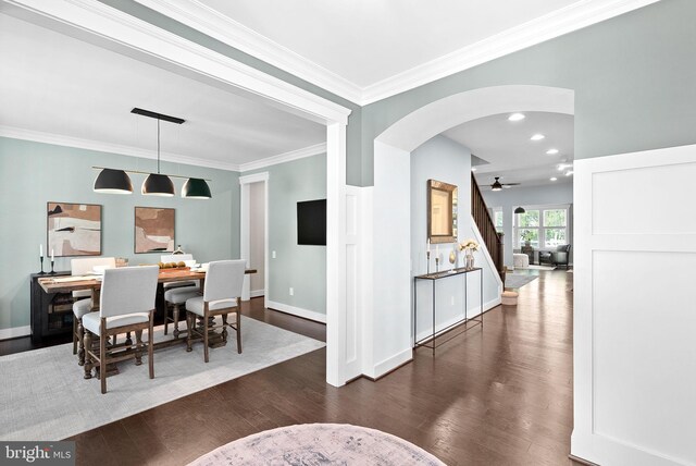 dining room featuring crown molding, arched walkways, dark wood finished floors, and stairway