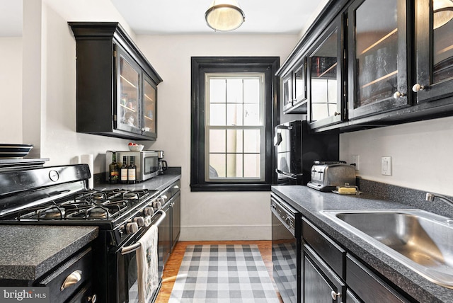 kitchen featuring dark countertops, glass insert cabinets, baseboards, a sink, and black appliances