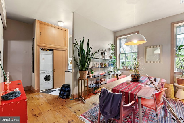 dining room featuring baseboards, a healthy amount of sunlight, stacked washer and clothes dryer, and hardwood / wood-style floors