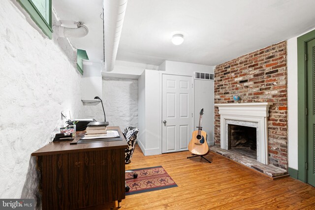 office area featuring a brick fireplace, wood finished floors, and visible vents