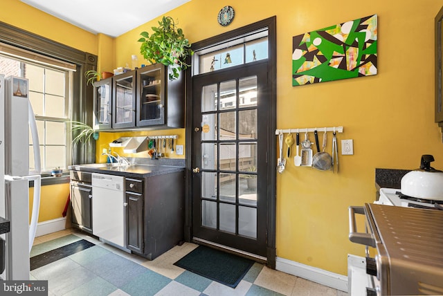 kitchen featuring baseboards, white dishwasher, a sink, and glass insert cabinets