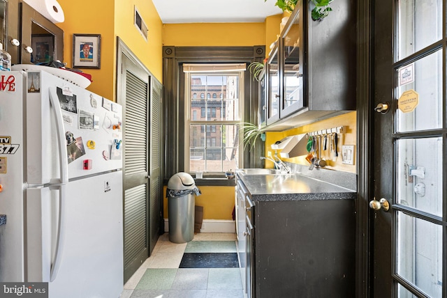 kitchen featuring baseboards, freestanding refrigerator, a sink, and dark countertops