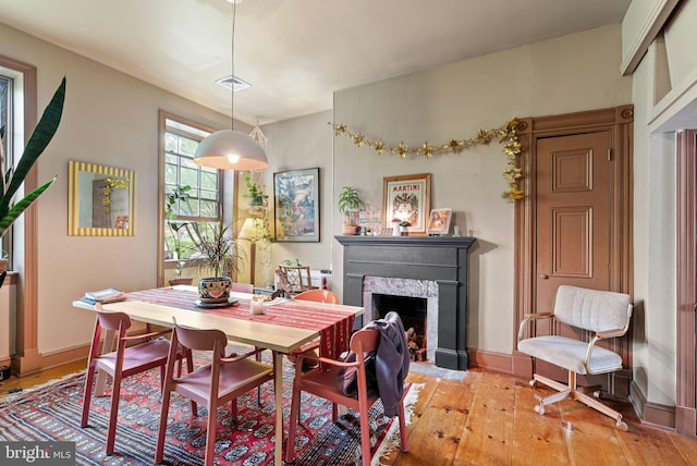 dining area featuring light wood-style floors, baseboards, visible vents, and a fireplace