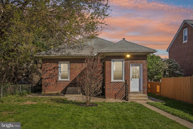 view of front of house featuring fence, entry steps, a yard, and brick siding