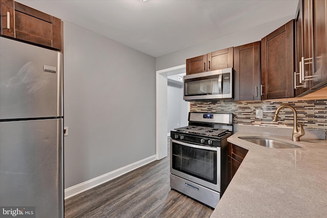kitchen featuring baseboards, dark wood-style flooring, a sink, decorative backsplash, and stainless steel appliances