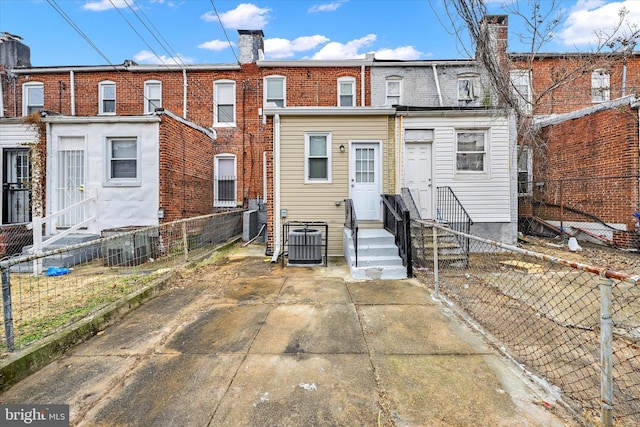rear view of property featuring cooling unit, a chimney, a fenced backyard, brick siding, and entry steps