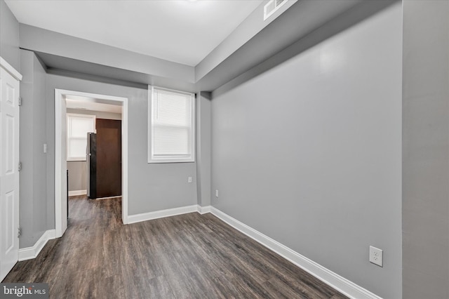 spare room featuring baseboards, dark wood-style floors, and visible vents