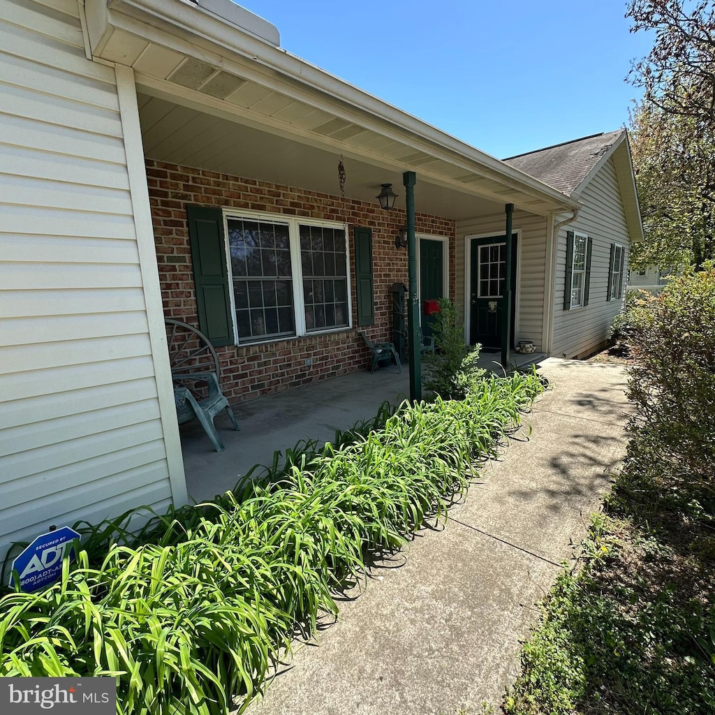 doorway to property featuring a porch and brick siding