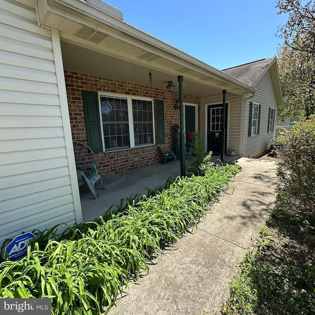 doorway to property featuring a porch and brick siding