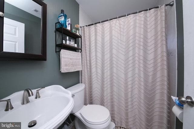full bathroom with toilet, a shower with curtain, visible vents, and a sink