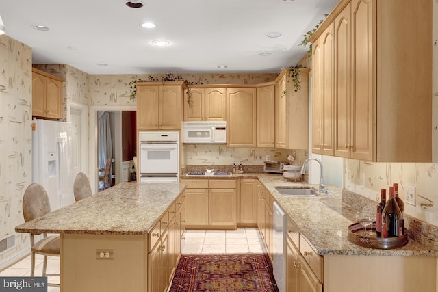 kitchen featuring light brown cabinetry, a sink, light stone counters, wallpapered walls, and white appliances