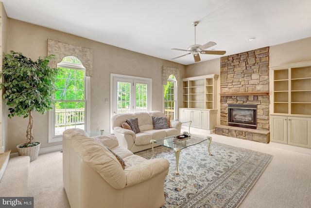carpeted living room with ceiling fan and a stone fireplace