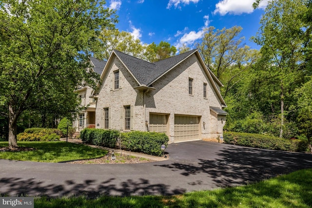 view of side of property featuring brick siding, an attached garage, driveway, and roof with shingles