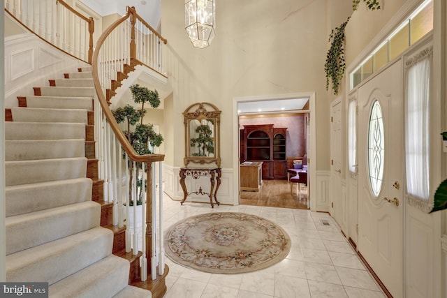entryway with a high ceiling, stairs, marble finish floor, and a decorative wall