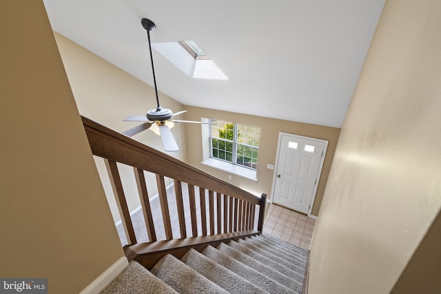 stairs featuring a ceiling fan, baseboards, and vaulted ceiling with skylight