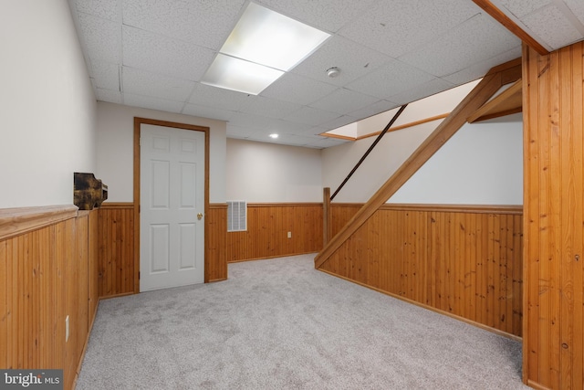 finished basement with visible vents, wood walls, a drop ceiling, a wainscoted wall, and carpet