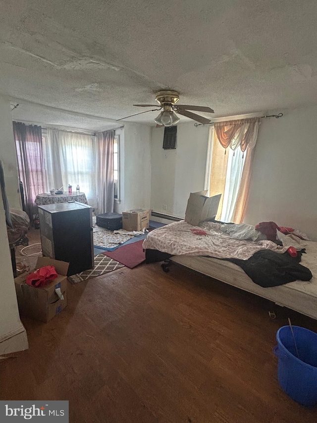 bedroom featuring a baseboard radiator, a textured ceiling, wood finished floors, and multiple windows