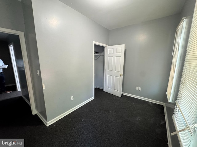 unfurnished bedroom featuring baseboards, dark colored carpet, and a closet