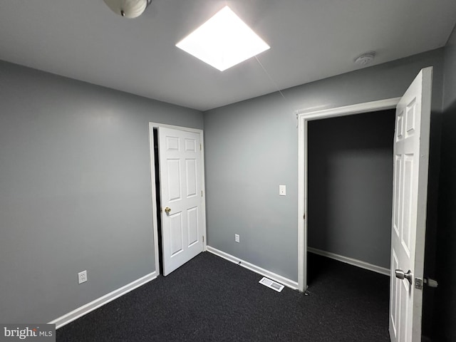 unfurnished bedroom with a skylight, dark carpet, and baseboards