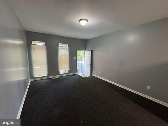 unfurnished room featuring baseboards and dark colored carpet