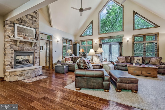living room with a ceiling fan, a stone fireplace, high vaulted ceiling, hardwood / wood-style flooring, and beam ceiling