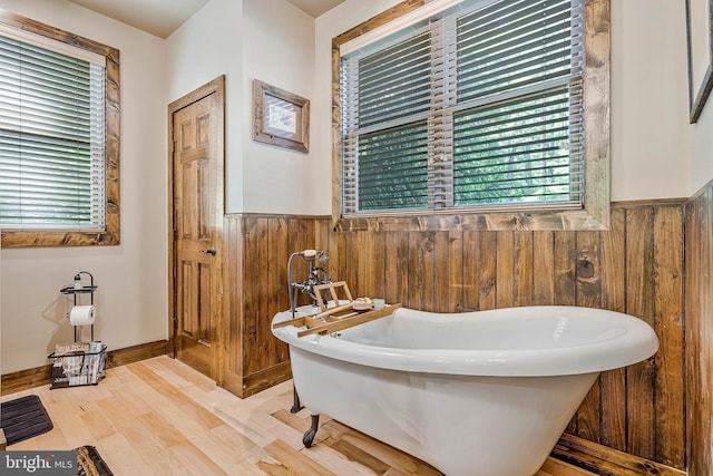bathroom featuring a soaking tub, wood walls, wood finished floors, and wainscoting