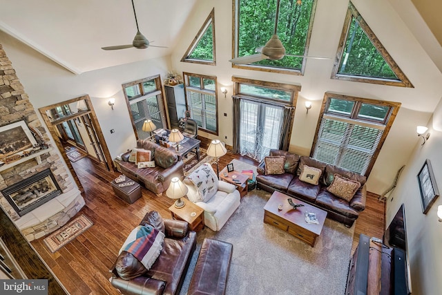 living room featuring ceiling fan, wood finished floors, a fireplace, and a high ceiling