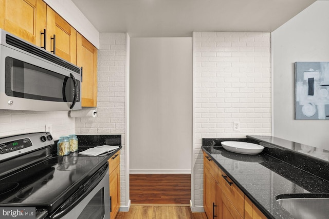 kitchen featuring stainless steel appliances, wood finished floors, dark stone counters, brown cabinetry, and baseboards
