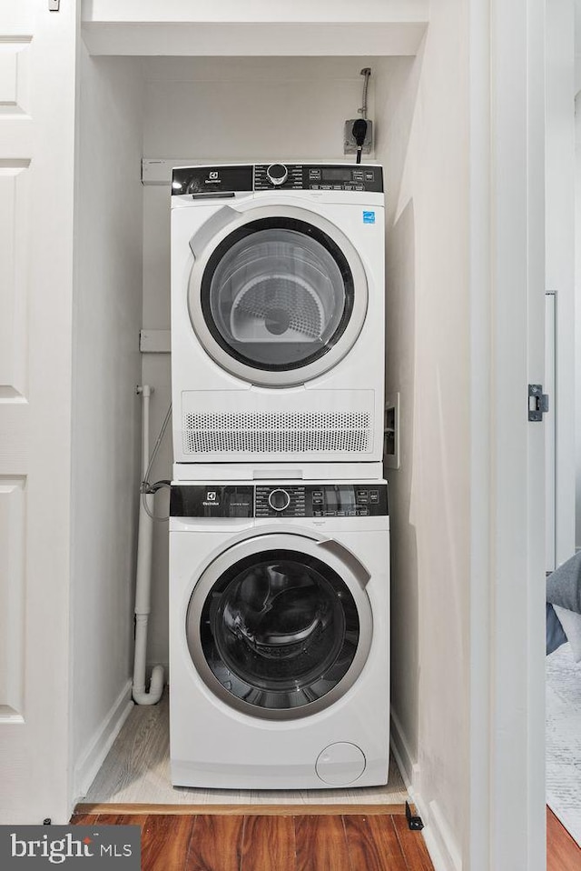 laundry area featuring stacked washer and clothes dryer, wood finished floors, and baseboards