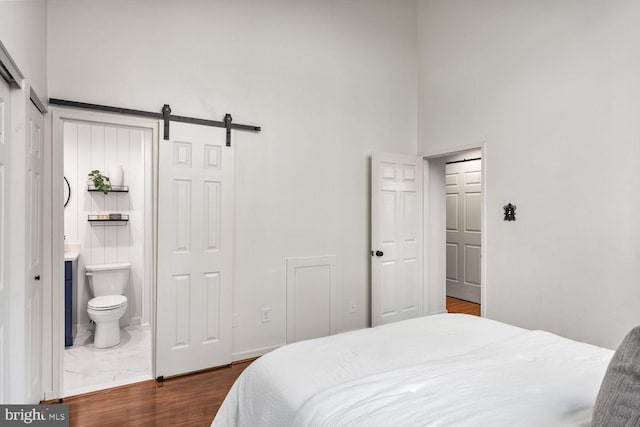 bedroom with a towering ceiling, a barn door, ensuite bath, and baseboards