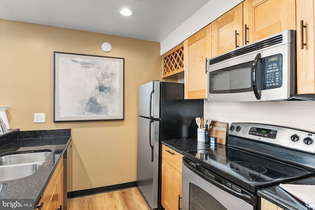 kitchen with stainless steel appliances, tasteful backsplash, light wood-style flooring, dark stone counters, and a sink