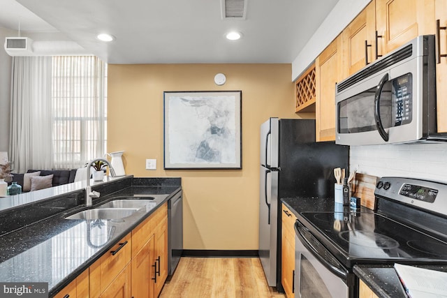 kitchen featuring stainless steel appliances, a sink, backsplash, light wood-type flooring, and dark stone counters